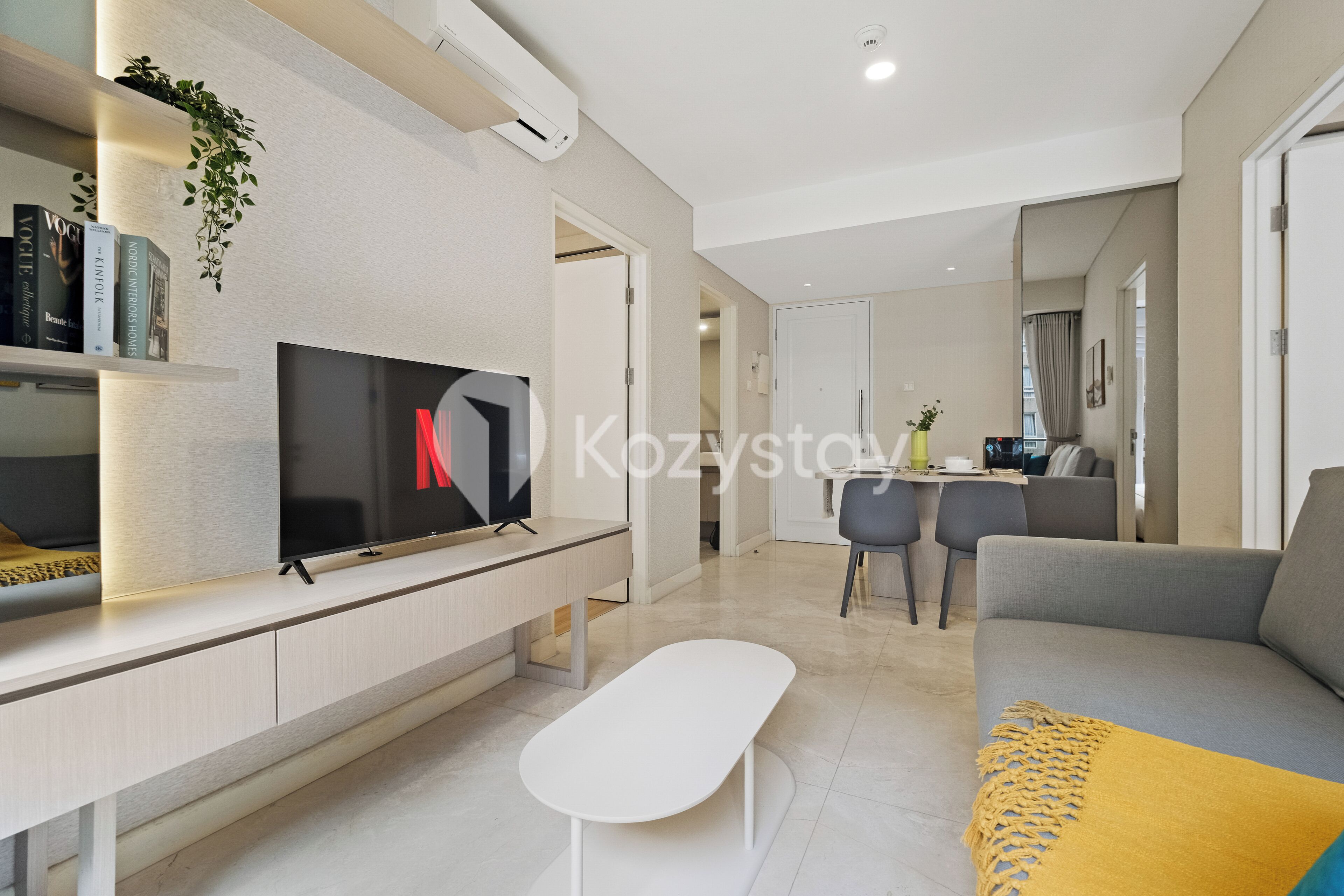 Een moderne woonkamer met een flatscreen televisie, een bank, een salontafel en een eethoek met stoelen.