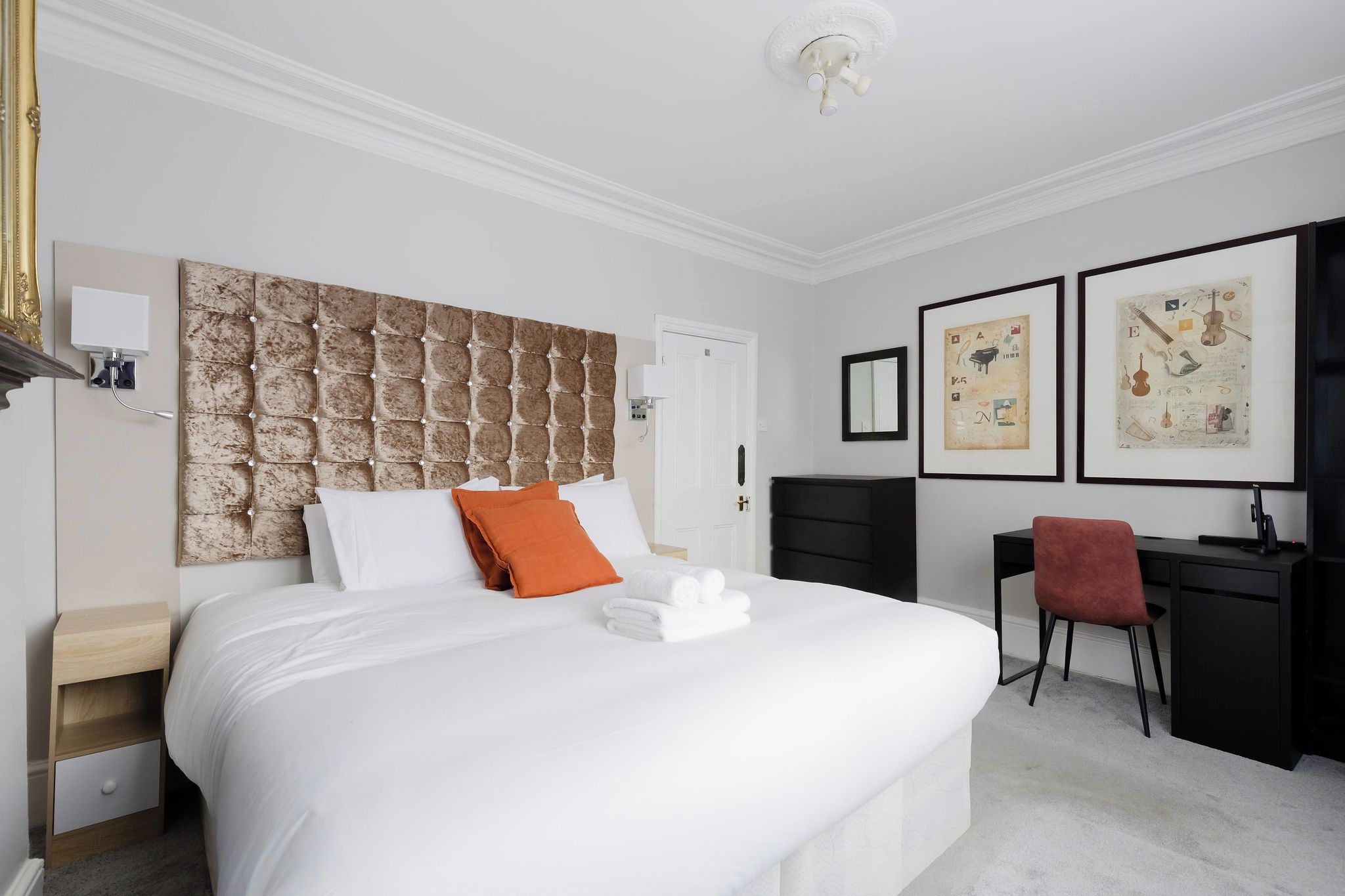 Ein Hotelzimmer mit einem großen Bett, einem Schreibtisch, einem Stuhl und Bildern an der Wand.