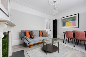 Un salon avec un canapé gris, une table basse en verre et une cheminée. On y trouve également un coin repas avec une table et des chaises.
