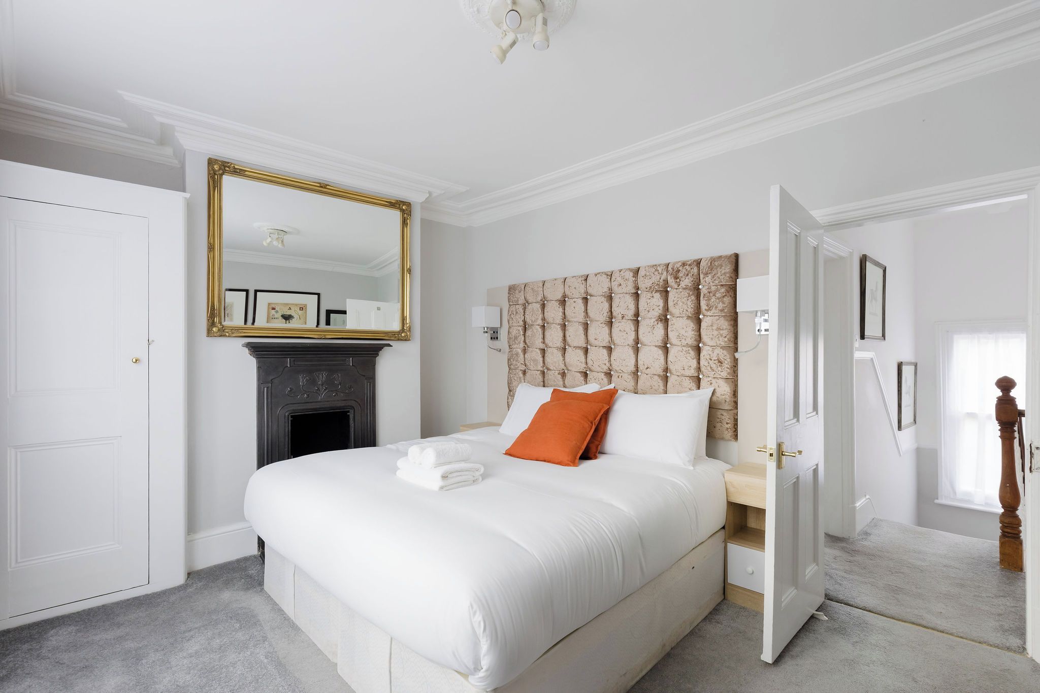 A hotel room with a large bed, a fireplace, a mirror, and a door leading to another room.
