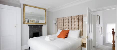 A hotel room with a large bed, a fireplace, a mirror, and a door leading to another room.