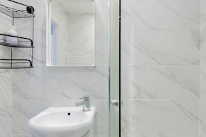 Een badkamer met een wit wastafelmeubel, een glazen douchecabine en een wand met een marmerprint.