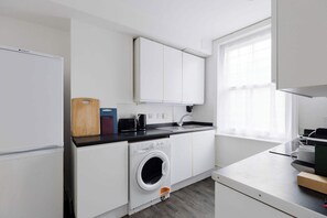 Een kleine keuken met een wasmachine, een spoelbak en een raam met gordijnen.