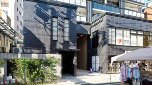 A modern building with a large entrance, a covered outdoor area with clothing, and a sign indicating a bookstore. - CREST Nishijin (Fukuoka)