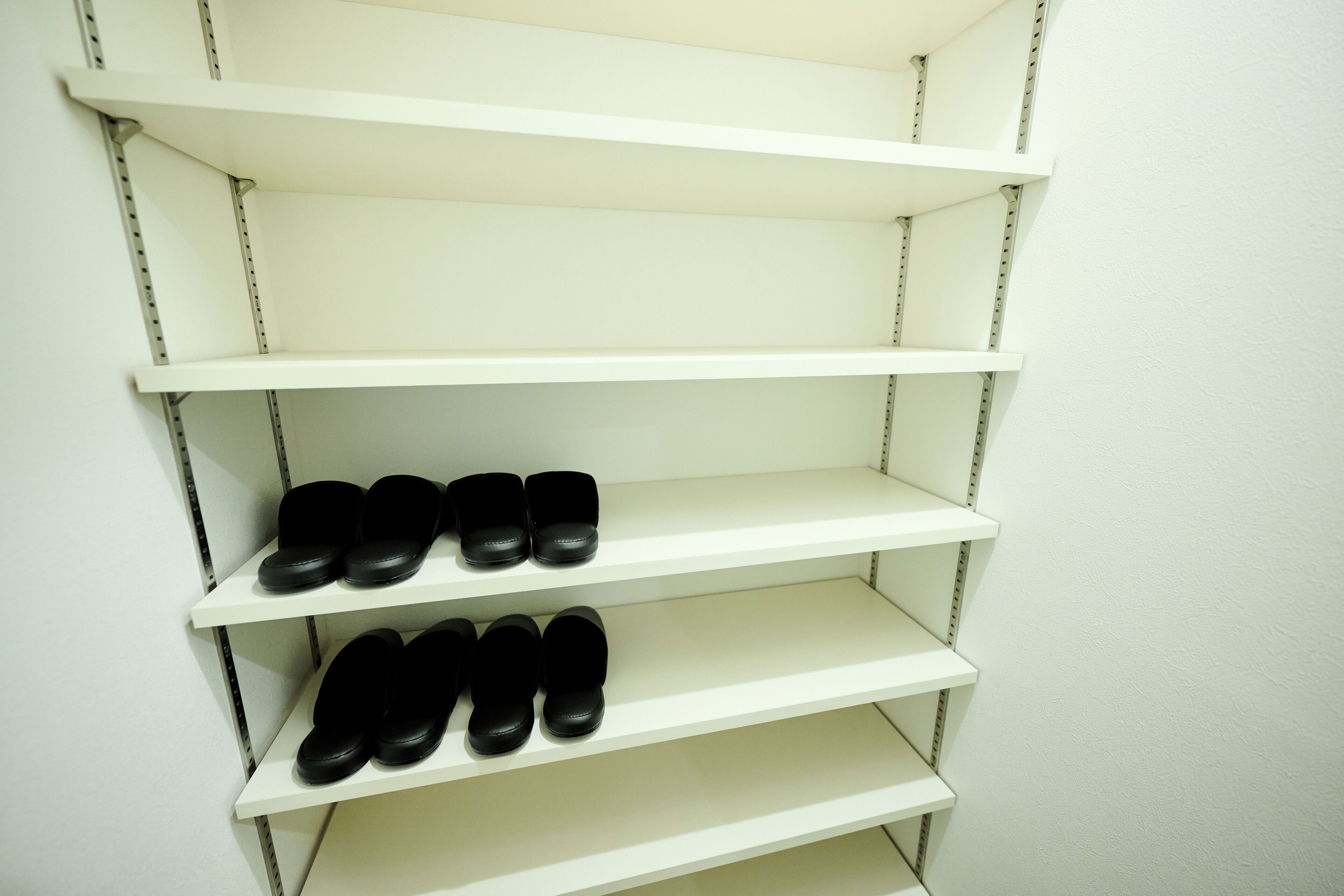 A set of white shelves with black shoes on the bottom shelf.