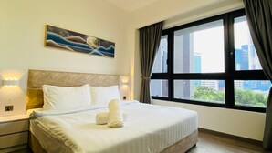 Quarto de hotel com uma cama grande, vista da cidade pela janela e um quadro na parede.