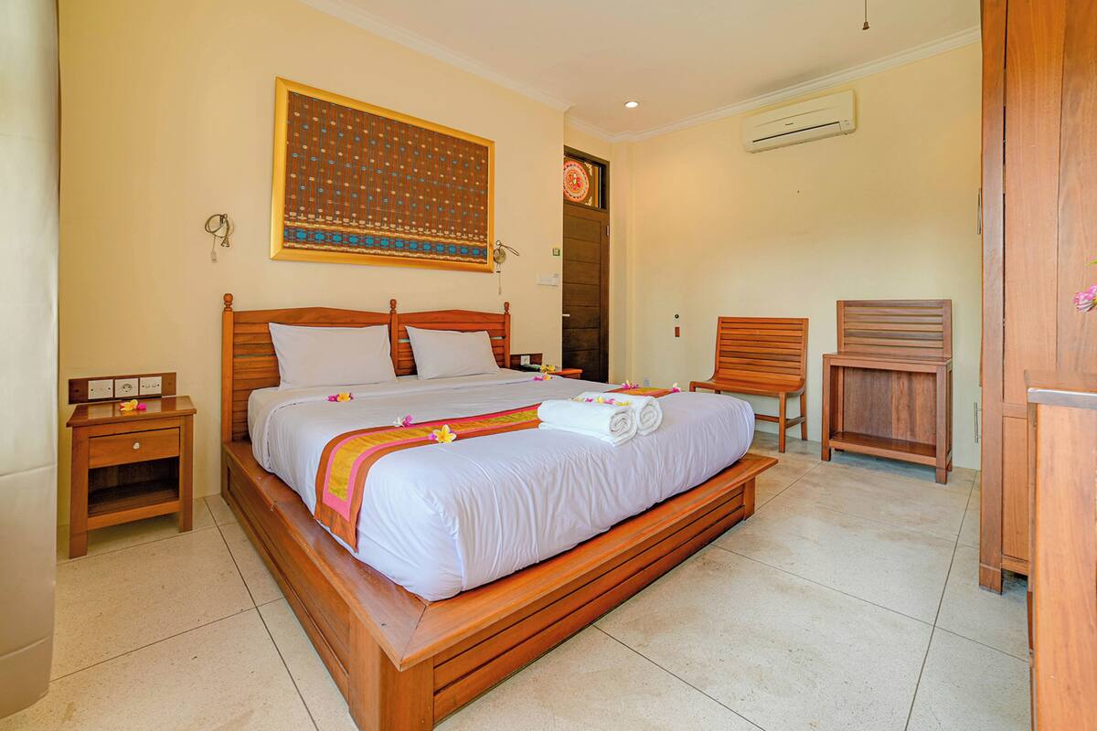 A large bed with a wooden frame, a nightstand, a chair, and a desk.