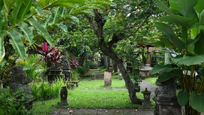 A garden pathway with stone lanterns and statues, surrounded by lush greenery. - Suly Resort Ubud (Ubud)