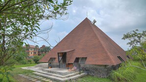 A pyramid-shaped building with a stone base and a red roof, surrounded by greenery. - Suly Resort Ubud (Ubud)