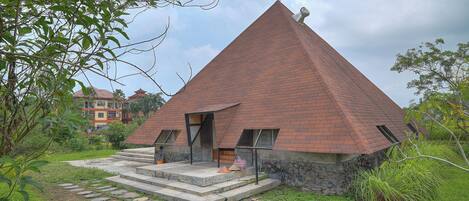 Un edificio a forma di piramide con base in pietra e tetto rosso, immerso nel verde.