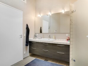 Une salle de bain moderne avec une porte blanche, un grand miroir, un lavabo et un meuble-lavabo en bois foncé doté de tiroirs.