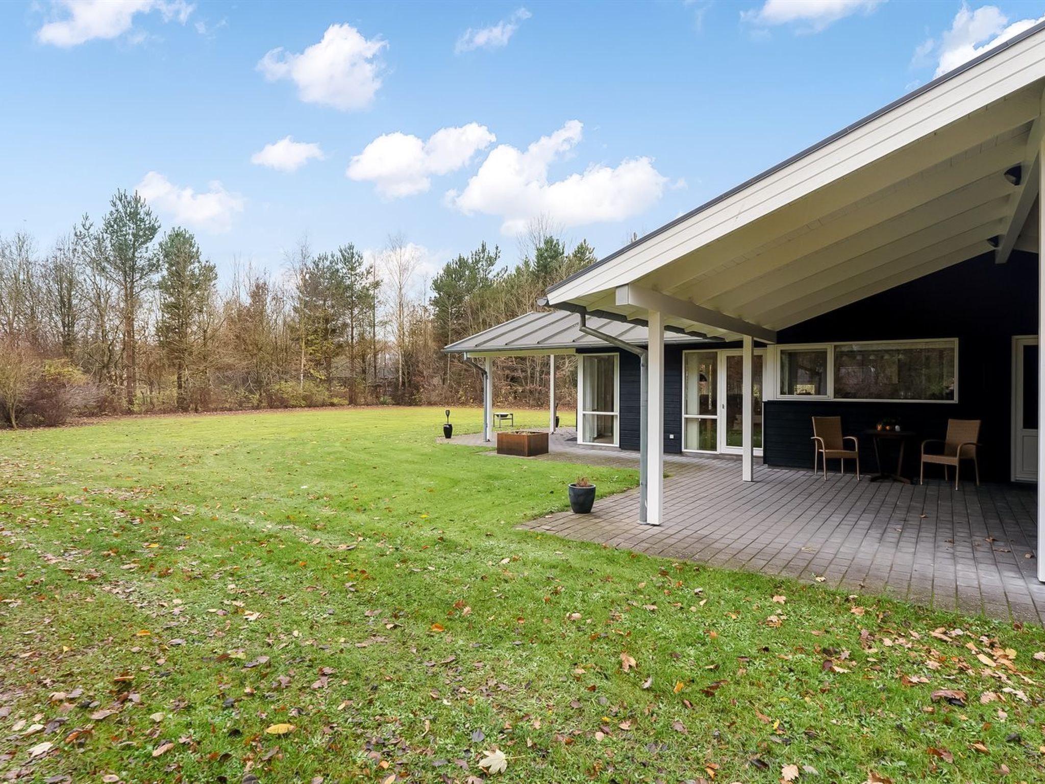 A modern house with a covered patio, a lawn, and a forest in the background.