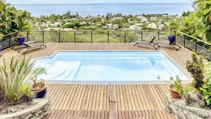A wooden deck with a swimming pool, lounge chairs, and potted plants. - Villa Bel Ocean - Piscine & Vue Mer Saint Gilles (Saint-Paul)