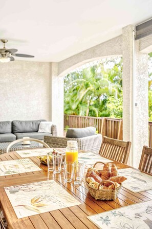 Une table de salle à manger en bois, avec un panier de croissants, un verre de jus d’orange et un menu.