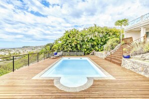 Une terrasse en bois avec une piscine rectangulaire, entourée d’un mur de pierre et d’une rambarde en métal.