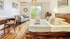 A bedroom with a bed, a desk, a chair, a sofa, and a balcony with a view of greenery. - Villa Bel Ocean - Piscine & Vue Mer Saint Gilles (Saint-Paul)