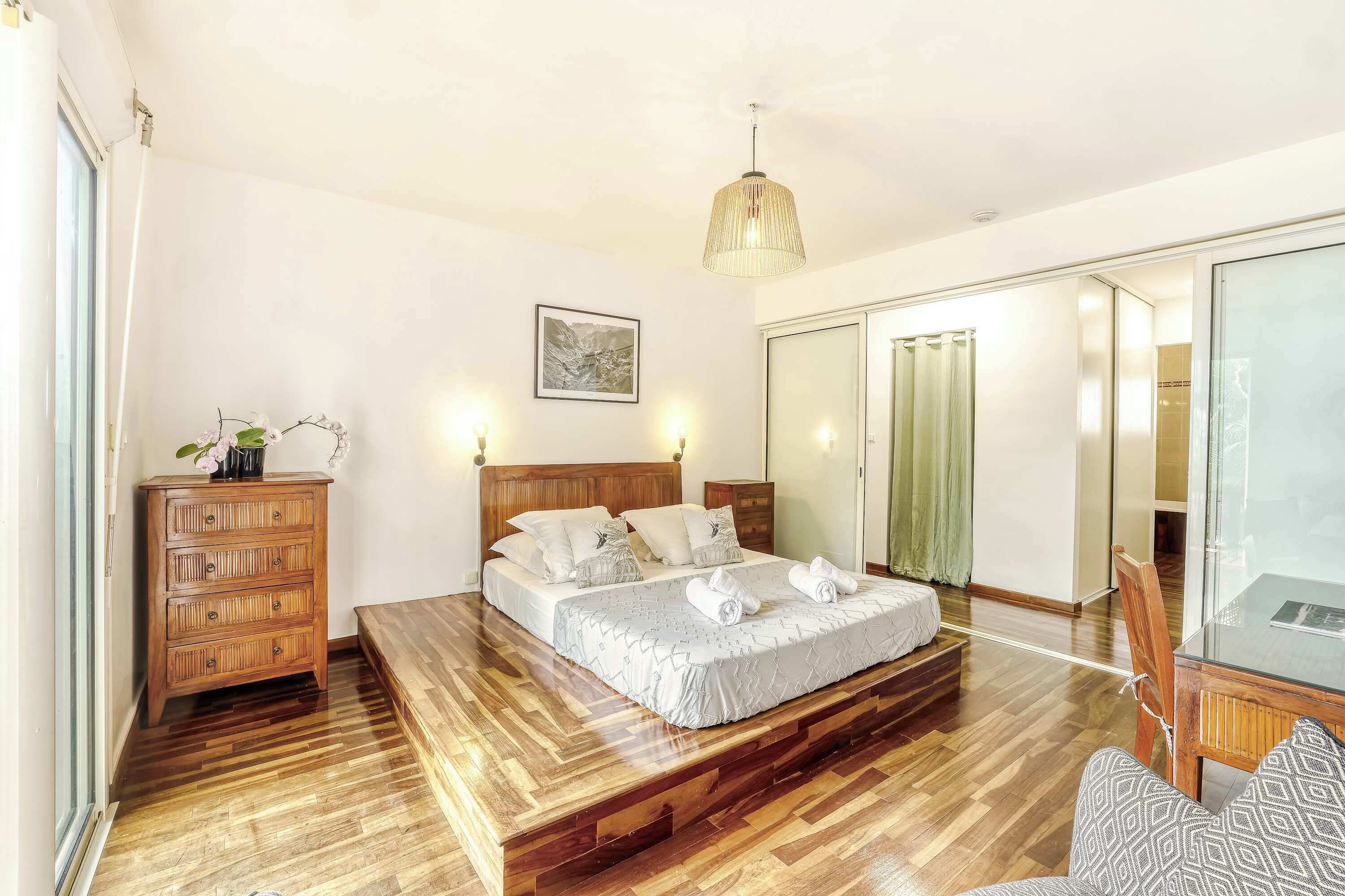 Un dormitori amb llit de fusta, una tauleta de nit, un armari i una cabina de dutxa de vidre.