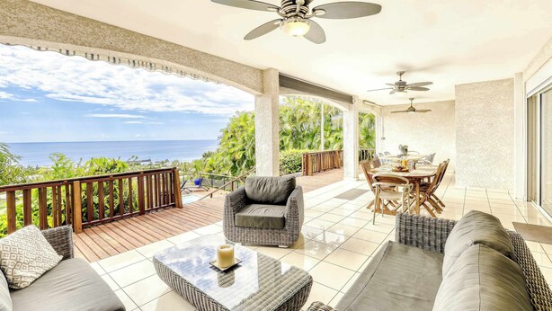 A covered outdoor area with a view of the ocean, furnished with wicker sofas, a glass coffee table, and ceiling fans. - Villa Bel Ocean - Piscine & Vue Mer Saint Gilles (Saint-Paul)