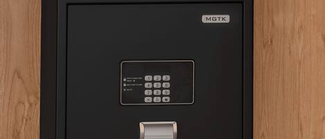 A black safe with a keypad and a brand label 'MGTK' on a wooden shelf.