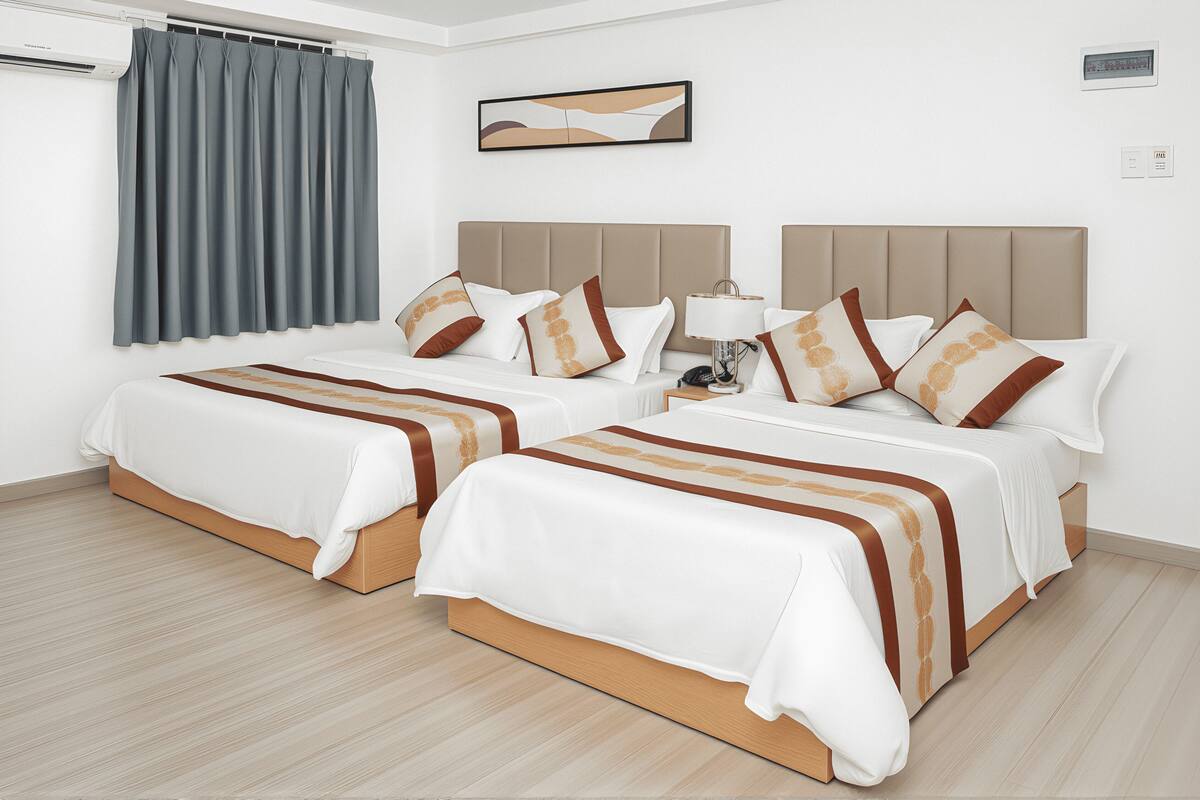 Une chambre d’hôtel avec deux lits, une table de chevet avec une lampe, un climatiseur fixé au mur et une fenêtre avec des rideaux.
