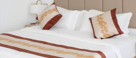 A neatly made bed with white bedding and decorative pillows, a bedside table with a lamp, and a headboard.