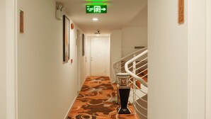 Un pasillo con alfombra estampada, una puerta blanca al final y una escalera con barandilla.