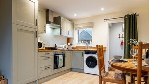 Una cocina compacta con lavadora, una mesa de comedor con sillas y una ventana con cortinas.