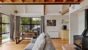 A cozy living room with a sofa, a dining table, and a fireplace. - Arc House | 5min to Town • Spacious Loft House (Queenstown)