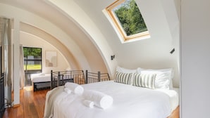 A bedroom with a large bed, a skylight, and a view of greenery outside. - Arc House | 5min to Town • Spacious Loft House (Queenstown)