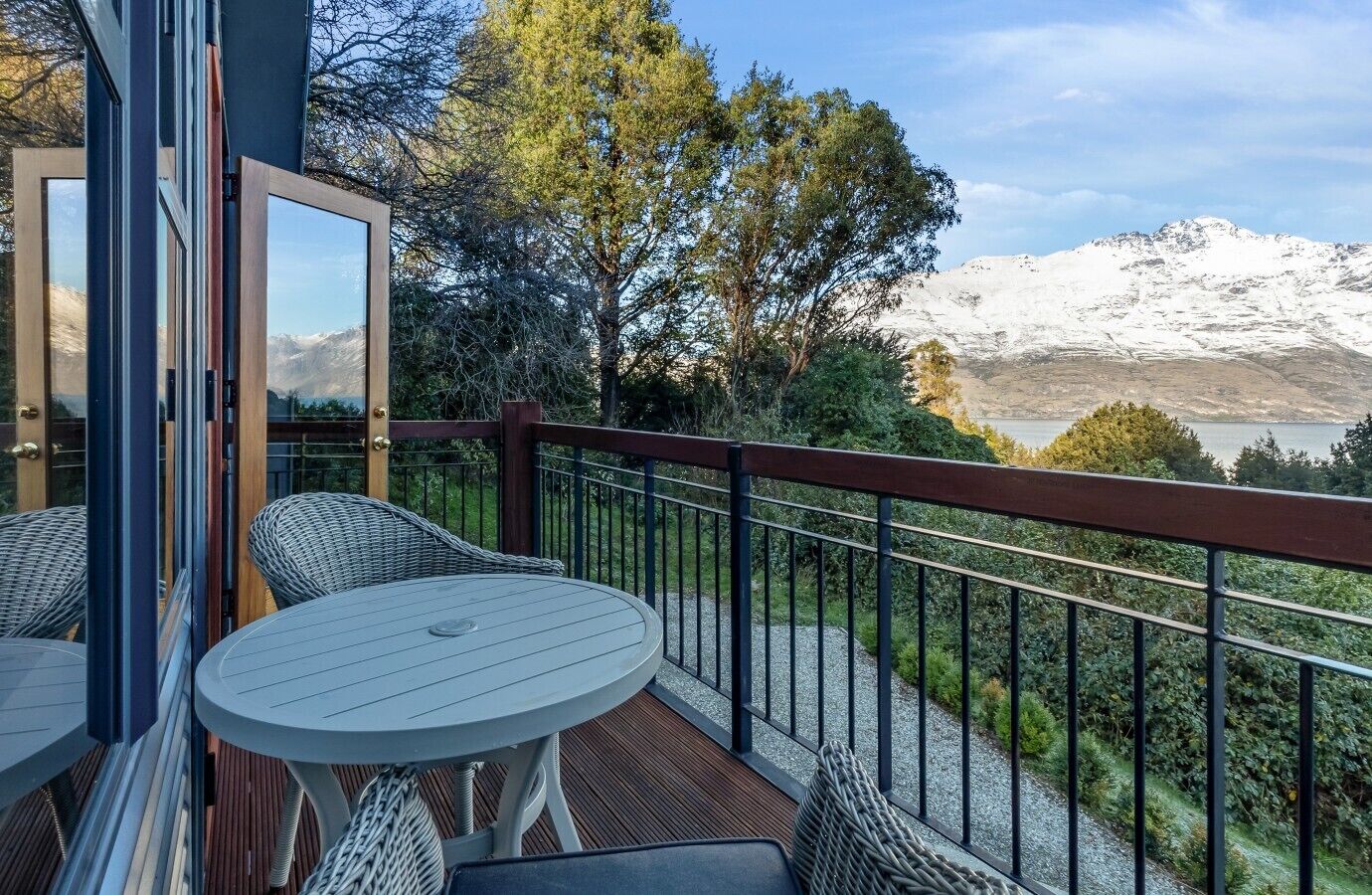 Un balcon offrant une vue sur des montagnes enneigées, une terrasse en bois et des meubles en osier.