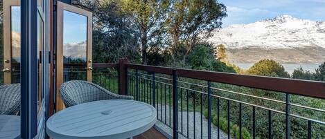 Un balcon offrant une vue sur des montagnes enneigées, une terrasse en bois et des meubles en osier.