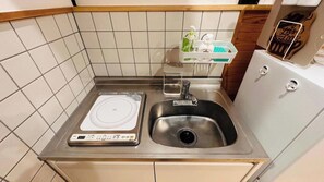 Eine kompakte Küche mit integriertem Induktionskochfeld, einer Spüle aus Edelstahl und einem kleinen Ablagebereich für Toilettenartikel.