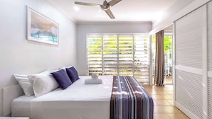 Ein Schlafzimmer mit einem Bett, einem Deckenventilator, einem Fenster mit Jalousien und Blick ins Freie.
