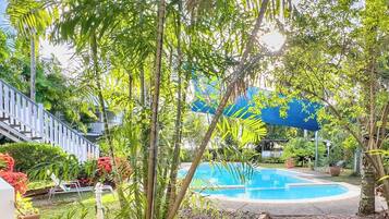 A pool area with a blue umbrella, surrounded by tropical plants and a stone pathway.