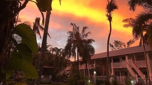 Een hotel met zwembad, omringd door palmbomen en een zonsondergang.