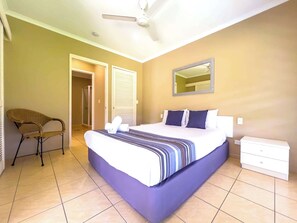 Een hotelkamer met een bed, een stoel, een nachtkastje, een spiegel en een plafondventilator.