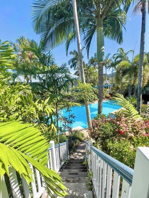 A pool area with a staircase leading down to a pool, surrounded by palm trees and tropical plants. - Poolside Garden Apt at Mango House, Whitsundays (Airlie Beach)