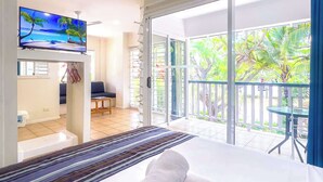A hotel room with a large bed, a TV on the wall, and a balcony with a view of greenery.