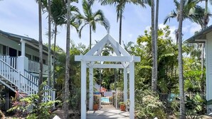 A wooden pathway leading to a white gazebo surrounded by palm trees and a pool. - Whitsundays Mango House Studio with Pool (Airlie Beach)
