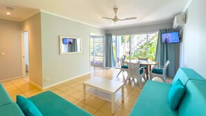 Una sala de estar con ventilador de techo, televisor, mesa de comedor con sillas y sofá.