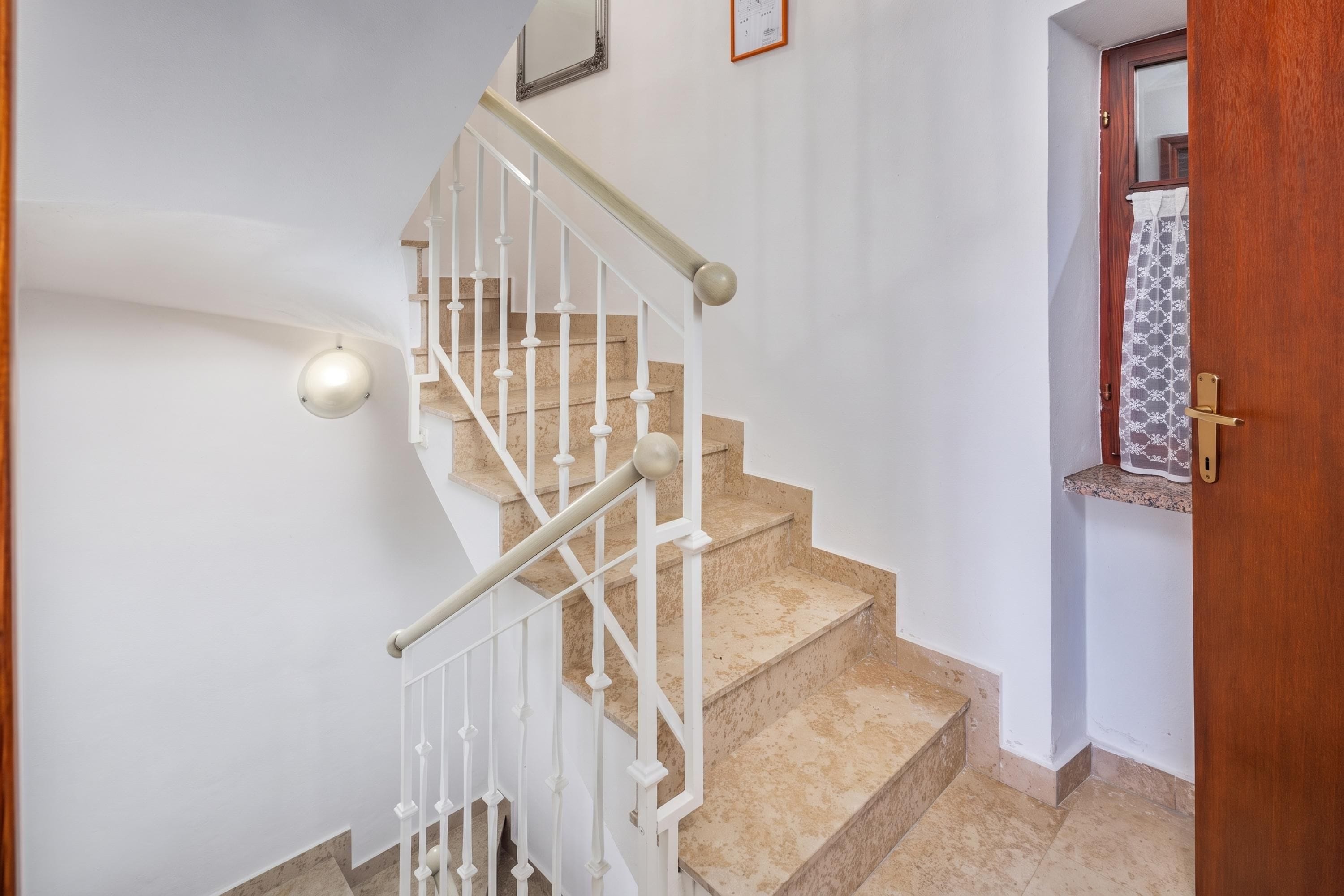 Una escalera con balaustres blancos y peldaños alfombrados en tono beige que conducen a una plataforma.
