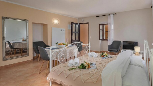A hotel room with a bed, a dining table with chairs, a TV, and a mirror. - Iva Apartments (Bale)