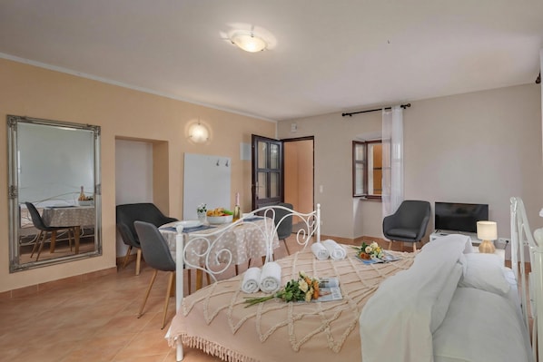 A hotel room with a bed, a dining table with chairs, a TV, and a mirror. - Iva Apartments (Bale)