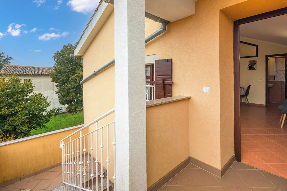 Un balcon d’habitation avec une balustrade blanche, une porte dotée de volets en bois et un sol carrelé.