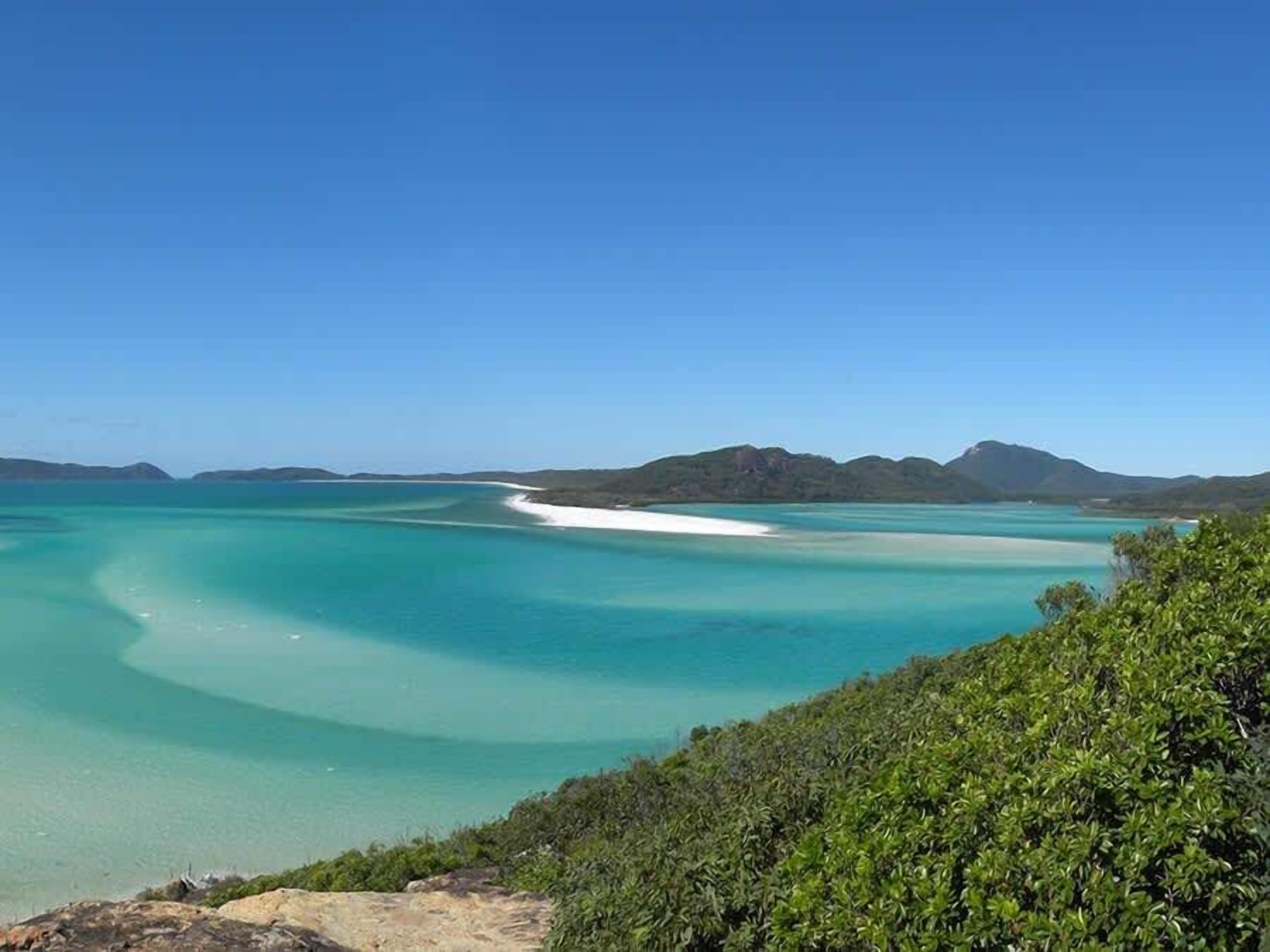 A coastal landscape with clear turquoise waters, a sandy beach, and green vegetation.