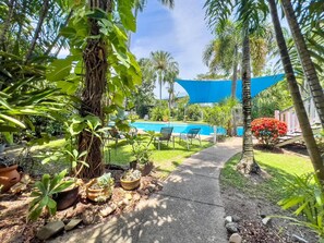 Ein Poolbereich mit blauer Markise, umgeben von tropischen Pflanzen und einem Weg zum Pool.