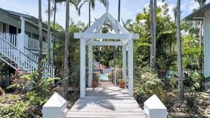 A wooden pathway leading to a white gazebo surrounded by palm trees and a pool. - Poolside Mango House Apartment, Whitsundays (Airlie Beach)