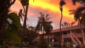 A hotel with a pool, surrounded by palm trees and a sunset sky. - Poolside Mango House Apartment, Whitsundays (Airlie Beach)