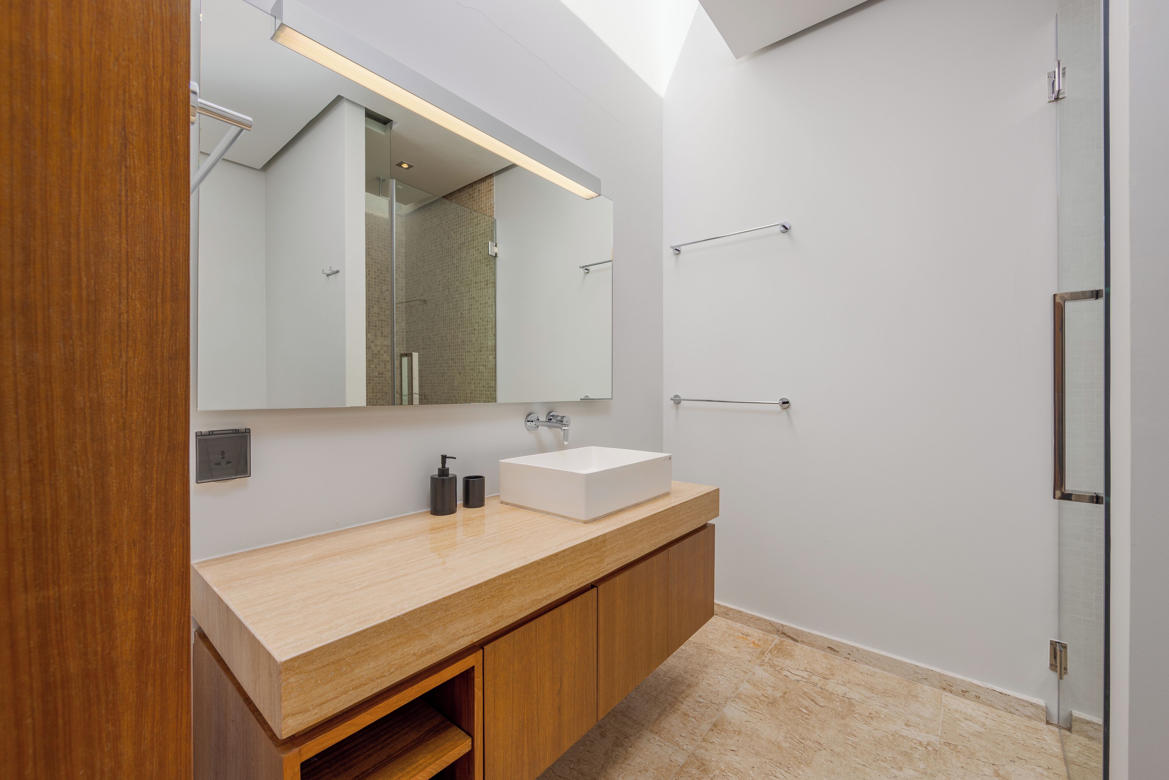 A modern bathroom with a wooden vanity, a large mirror, and a shower area.