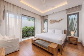 A modern bedroom with a large bed, a wooden bench, a chair, and a nightstand with a lamp. - Modern 3BR Villa Kaimana Private Pool (Thep Krasattri)